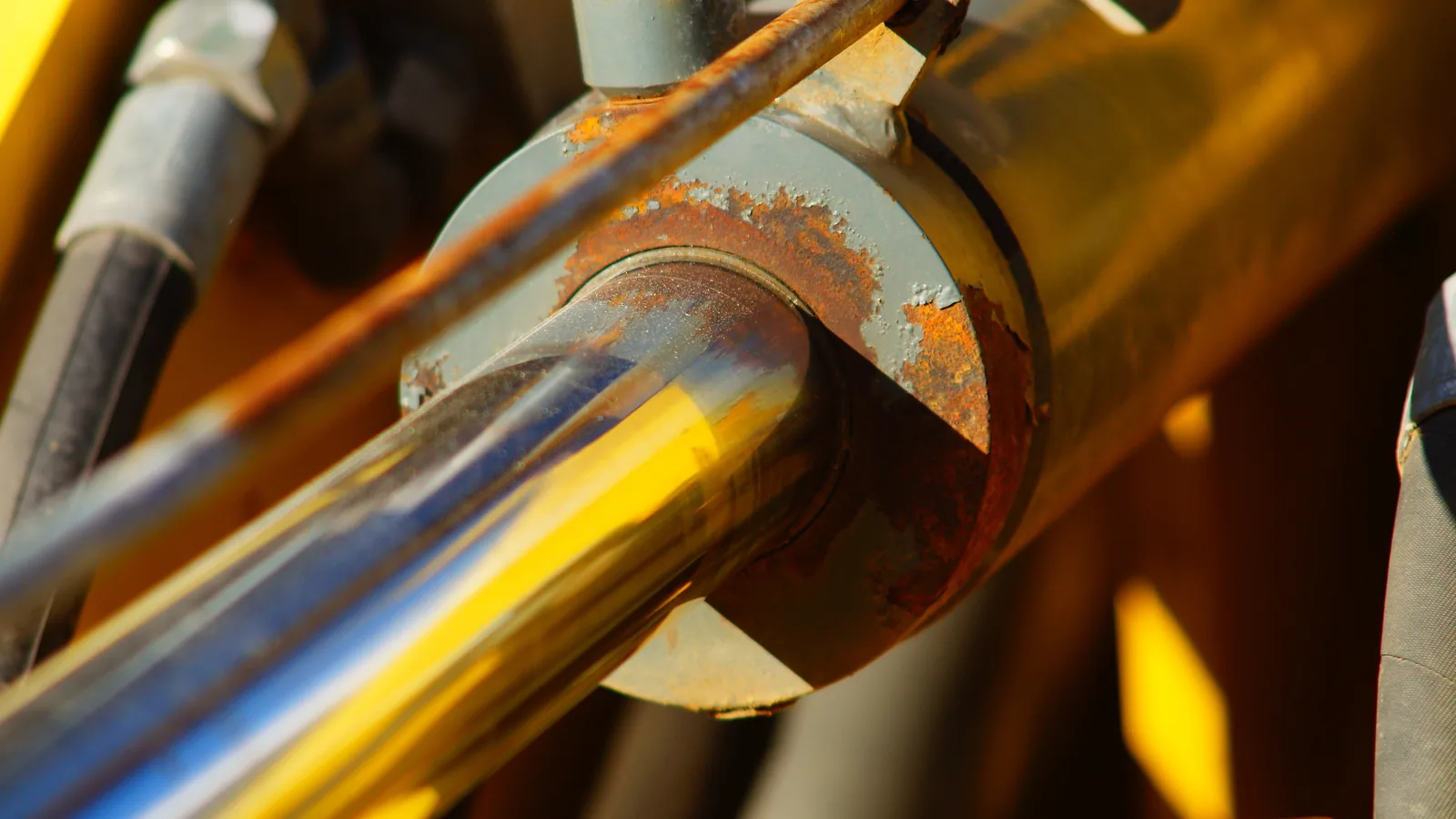 Stelo cromato con velo d'olio, uno dei segnali del cilindro idraulico che cede, sul braccio di un escavatore giallo in cantiere